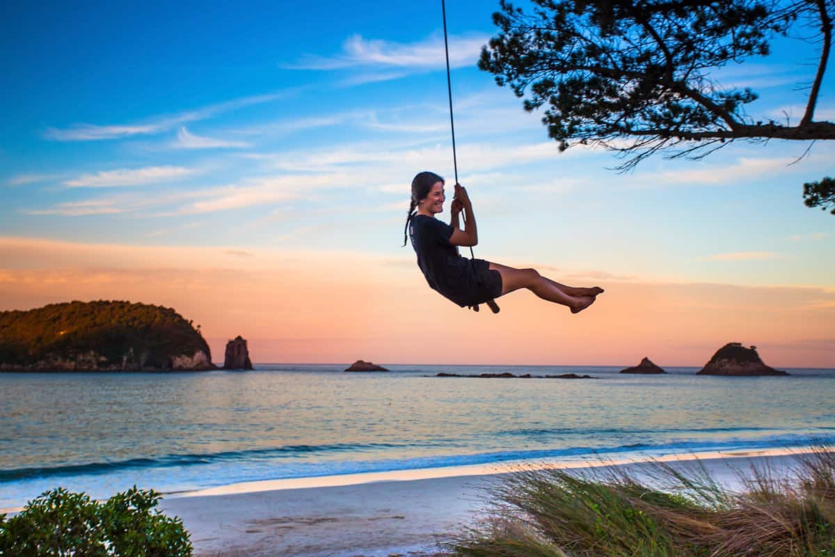 Voyageuse profitant du coucher du soleil tout en se balançant sur une corde attachée à une branche d'arbre.